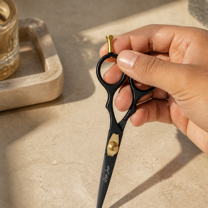 A hand lifting closed black and gold beard and moustache scissors