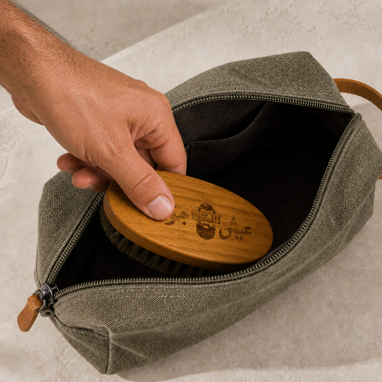 A hand packing the etched Diggn'It Bamboo Beard Brush into the Men's Travel Bag
